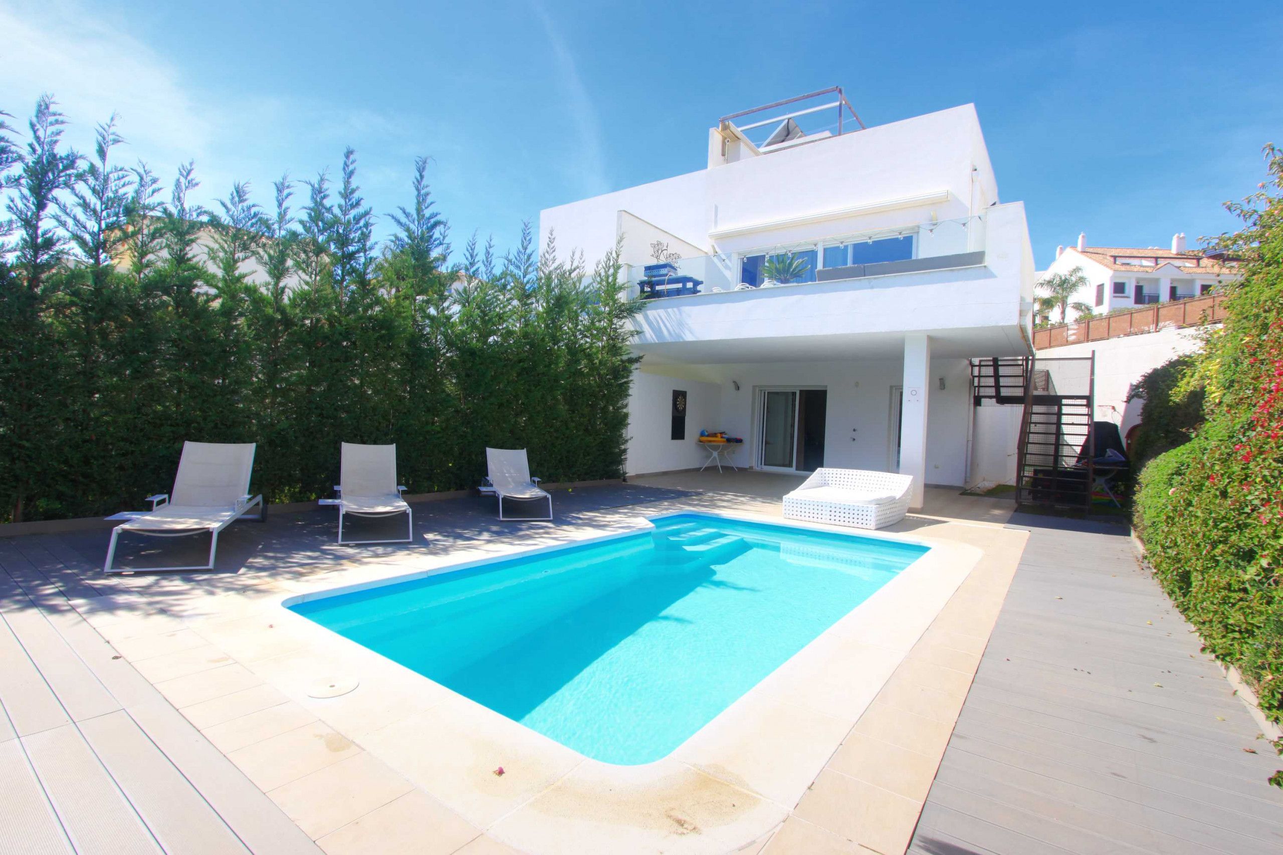 A modern two-story house with a swimming pool, lounge chairs, and a covered patio area.