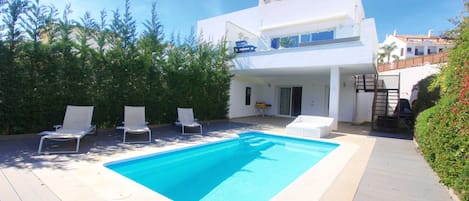 A modern two-story house with a swimming pool, lounge chairs, and a covered patio area.
