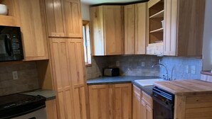 Eine Küche mit Holzausstattung, einem Herd, einer Mikrowelle, einem Spülbecken und einem Mülleimer.