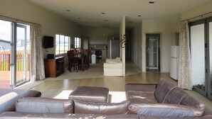 A spacious living room with a leather sofa, a dining area with a table and chairs, and a kitchen in the background. - Spacious Beach Home Away From Home (Tokerau Beach)
