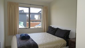 A bedroom with a bed, curtains, a window, and a view of the outside. - Spacious Beach Home Away From Home (Tokerau Beach)