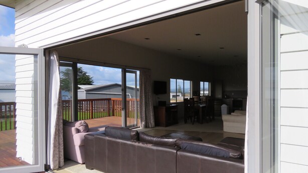 A spacious living area with a sliding glass door leading to a deck, a sectional sofa, and a dining area with a table and chairs. - Spacious Beach Home Away From Home (Tokerau Beach)