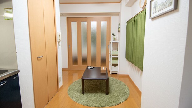 A narrow hallway with a wooden floor, a green rug, a wooden door, a white wall, a framed picture, and a clock. - Mell theater (Osaka)