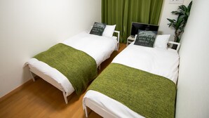 A room with two single beds, each with a green blanket and white bedding. There is a television on a side table next to one bed. - Mell theater (Osaka)