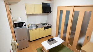 A compact kitchen with a microwave, stove, and sink. There is a small table with a power strip. - Mell theater (Osaka)