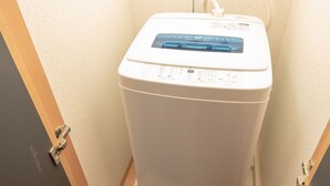 A white washing machine in a bathroom with beige walls and a wooden door frame. - Mell theater (Osaka)
