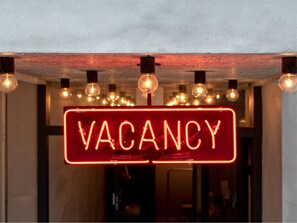 A neon sign reading "VACANCY" in a modern interior with exposed brick walls and hanging light bulbs. - EARTHMANS Amemura (Osaka)