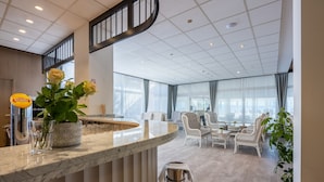 Un hall d’hôtel moderne avec un comptoir d’accueil en marbre, un espace salon et de grandes fenêtres.