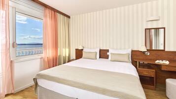 Habitació d'hotel amb un llit gran, una taula amb mirall i vista al mar per la finestra.