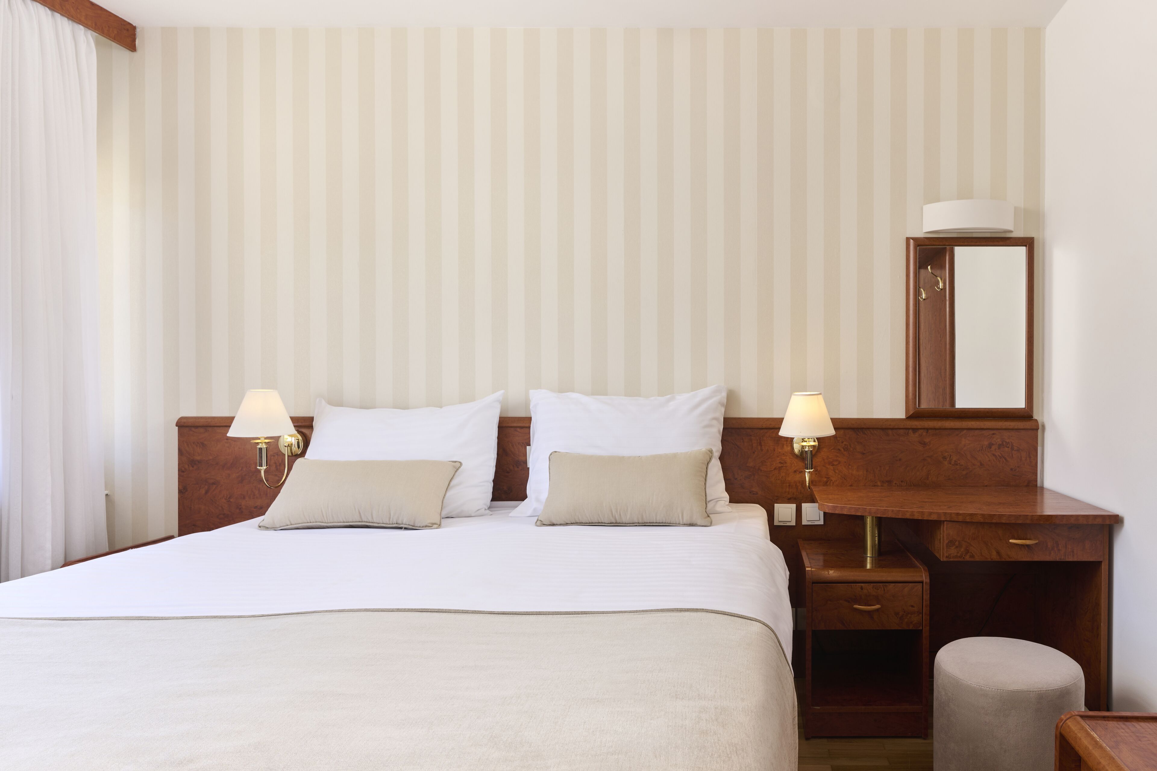 Habitación de hotel con una cama grande, dos mesitas de noche con lámparas, un escritorio de madera con un espejo y un taburete pequeño.
