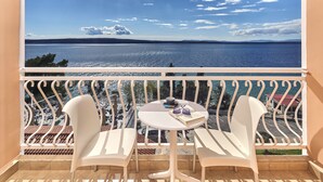 Un balcon avec des chaises blanches et une table, d’où l’on peut admirer un plan d’eau et un paysage lointain.