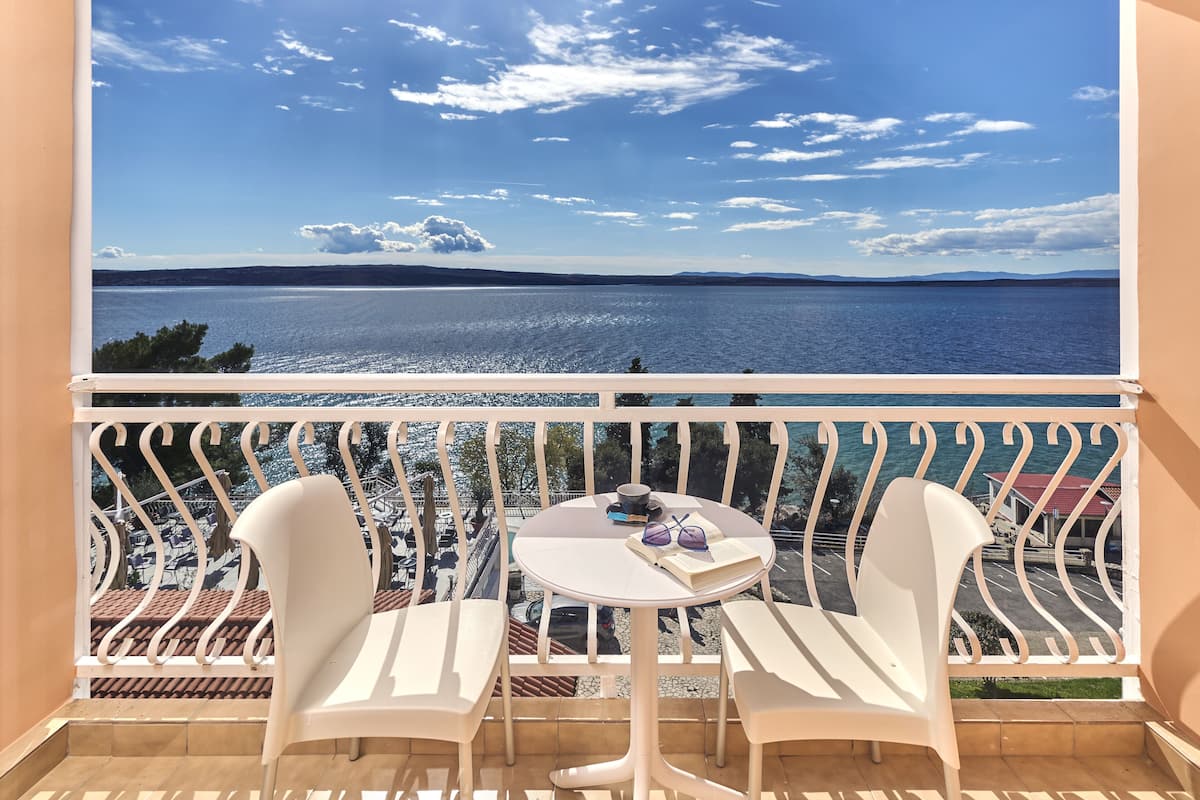 Un balcon avec des chaises blanches et une table, d’où l’on peut admirer un plan d’eau et un paysage lointain.