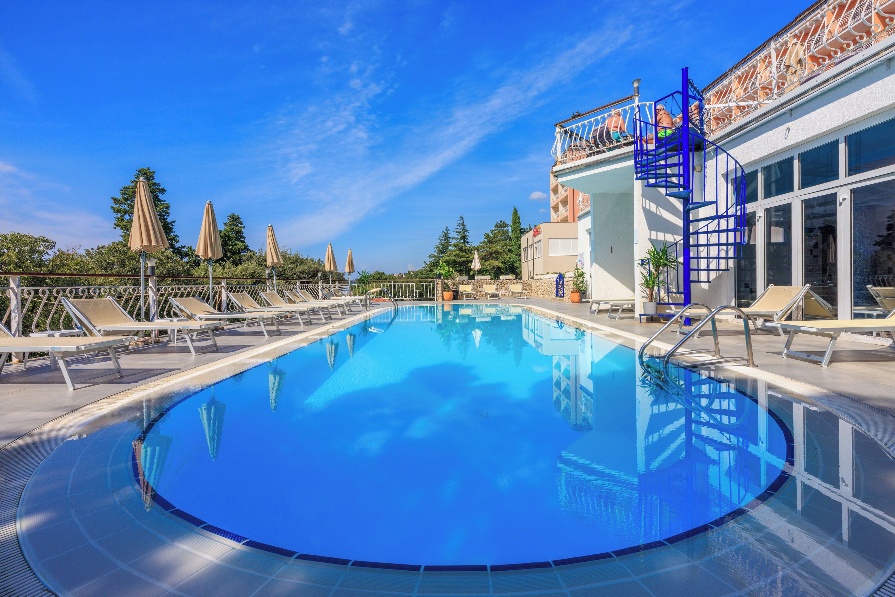 Ein klares, blaues Schwimmbecken mit Liegestühlen und einer blauen Treppe, die zu einer erhöhten Ebene führt.