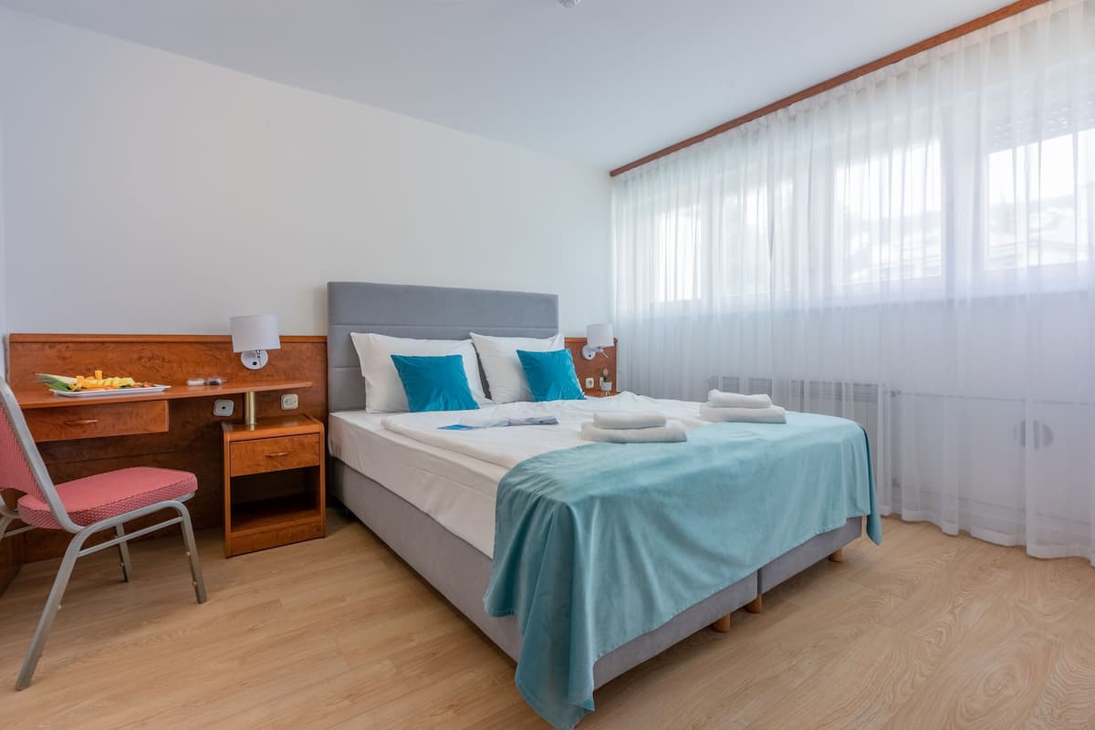 Une chambre à coucher comprenant un lit, un bureau, une chaise et une fenêtre avec des rideaux légers.