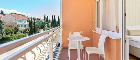 A balcony with a white table and chairs, a bed with a white headboard, and a view of the cityscape.