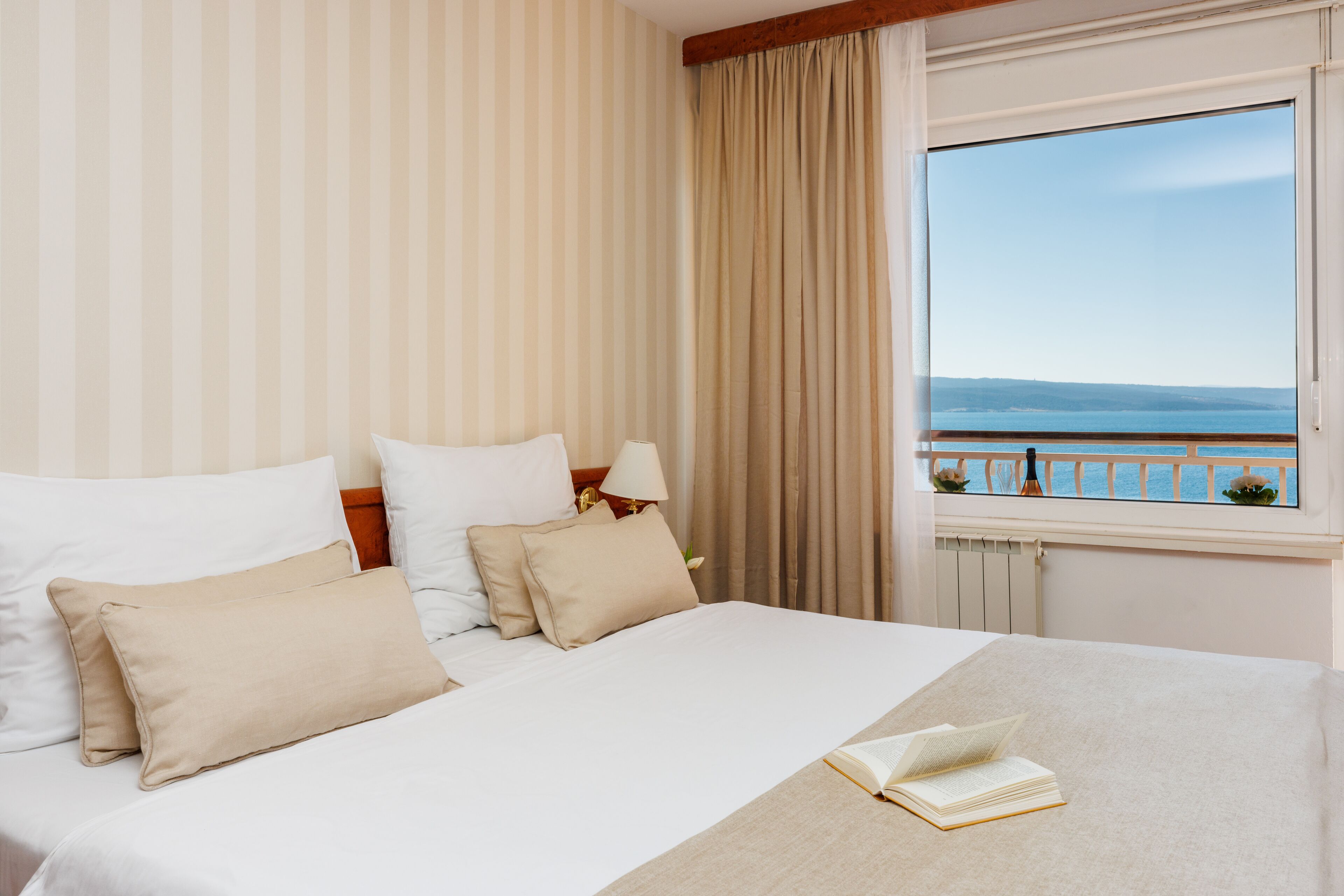 A hotel room with a bed, a window with a view of the sea, and a curtain.
