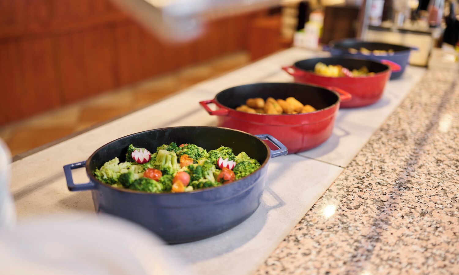 Een buffet met verschillende gerechten in potten, waaronder een schotel met broccoli en radijsjes.