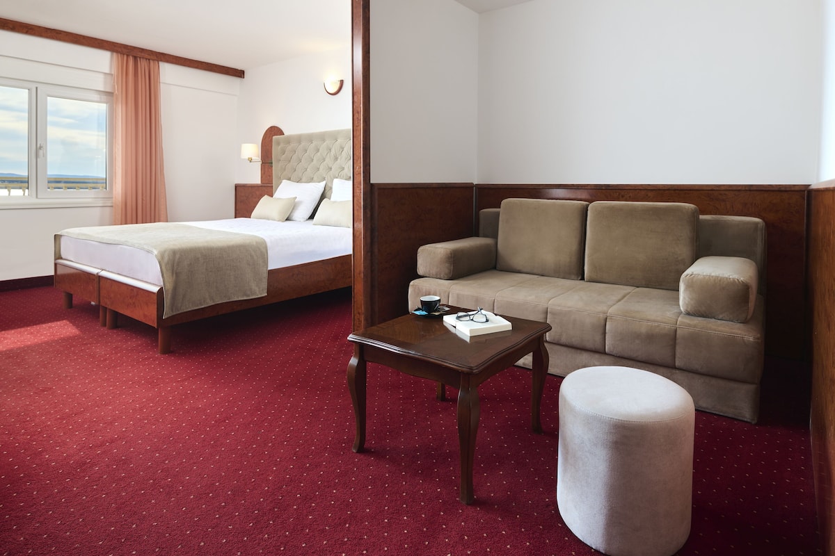 Une chambre d’hôtel avec un lit, un canapé, une petite table et un pouf rond.
