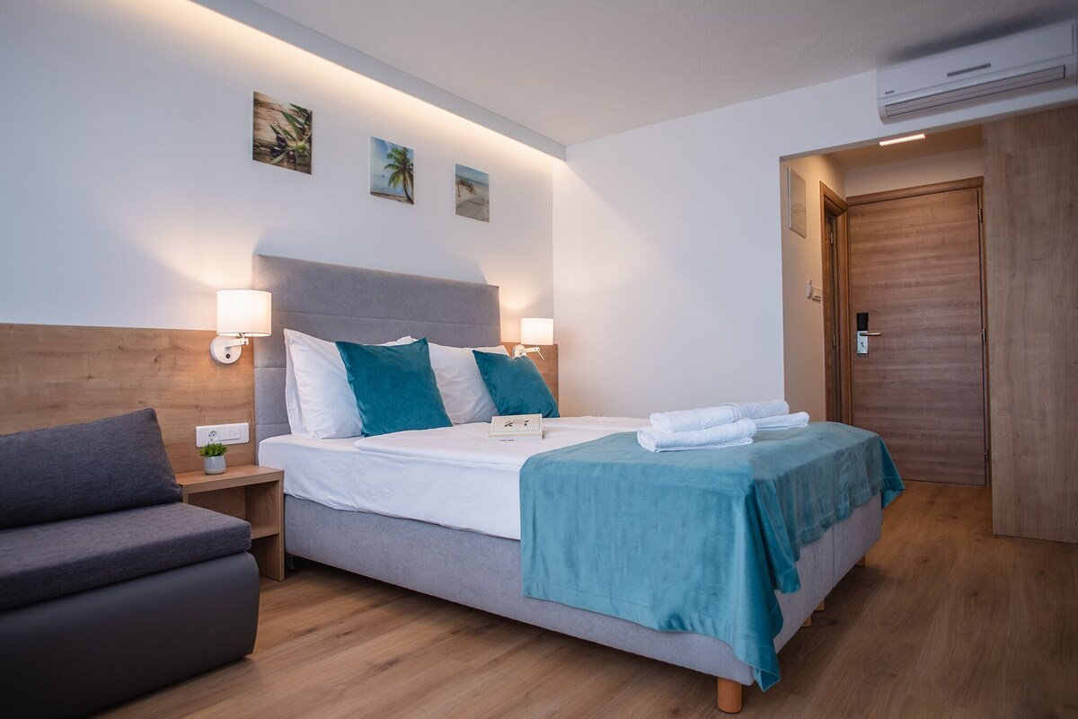 Une chambre d’hôtel moderne, équipée d’un lit, de tables de chevet, d’un canapé et d’une porte en bois.