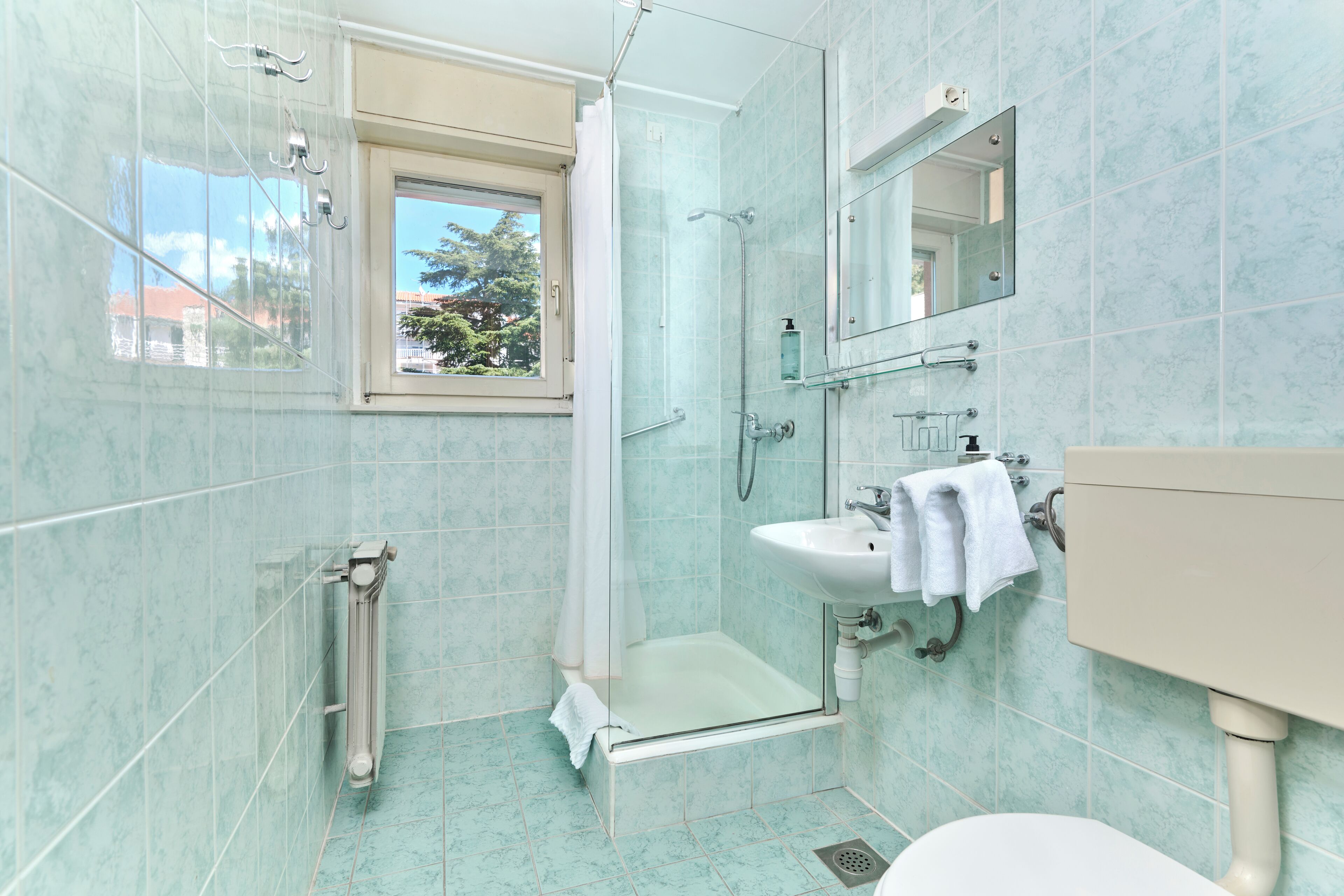 A bathroom with a glass shower enclosure, a sink with a mirror, and a window with a view of trees.