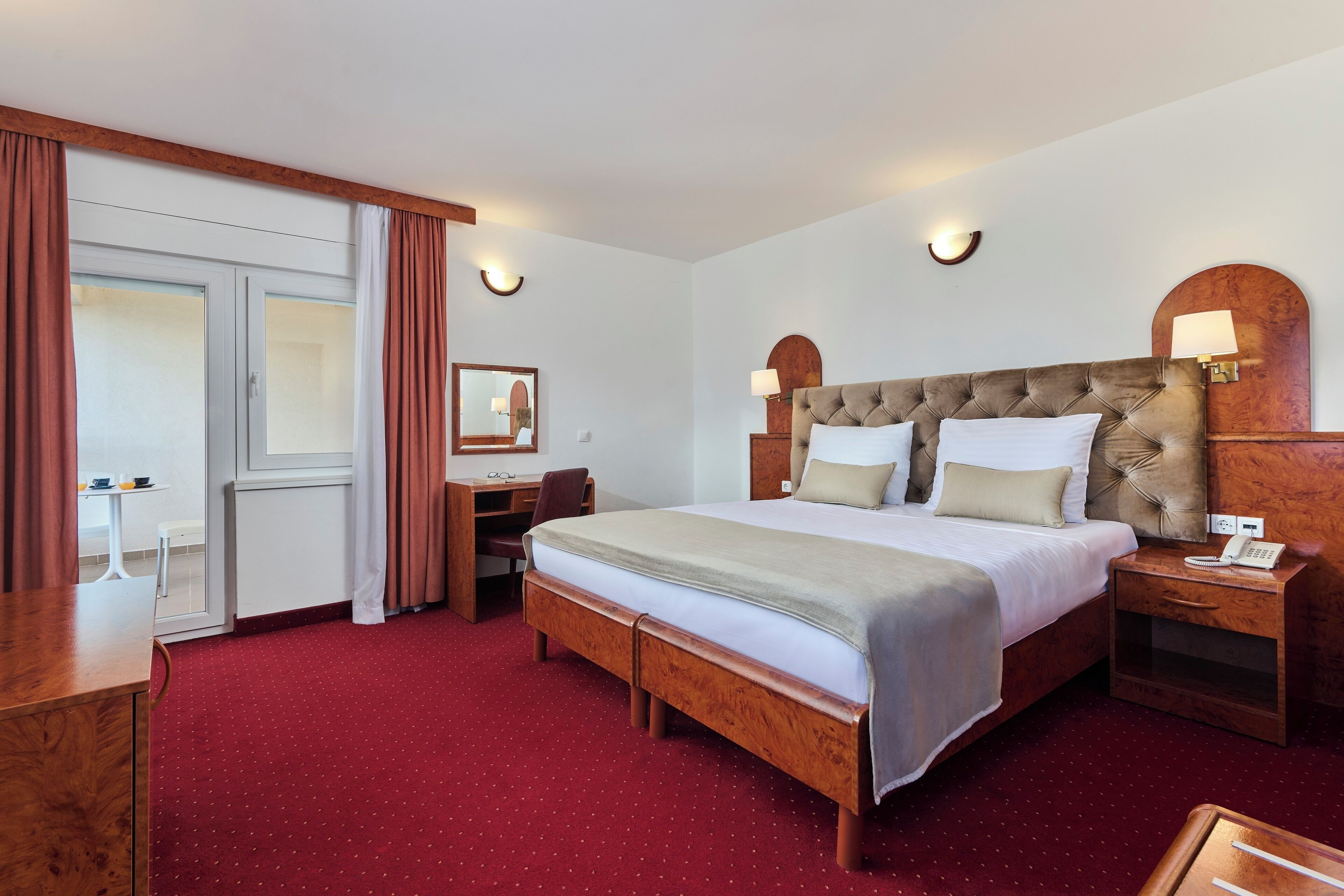 A hotel room with a large bed, wooden headboard, bedside tables, a desk, and a chair.