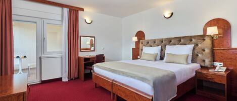 A hotel room with a large bed, wooden headboard, bedside tables, a desk, and a chair.