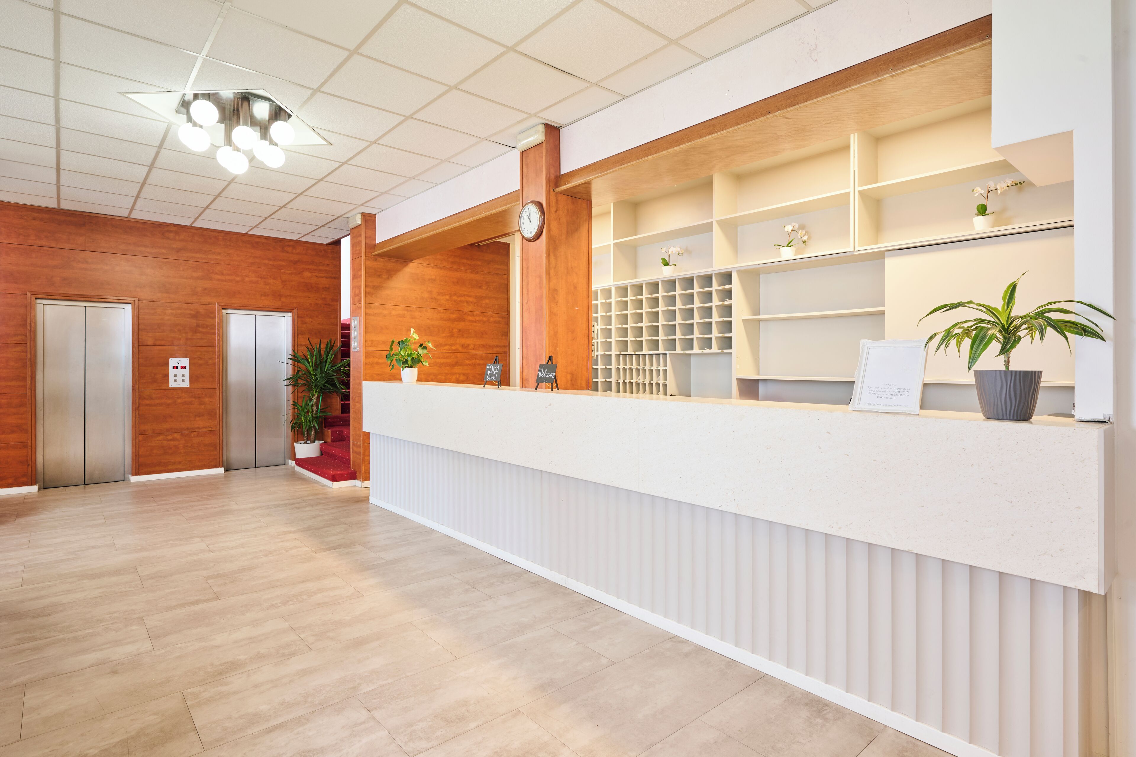 A reception area with a wooden floor, a reception desk, a clock, and potted plants.