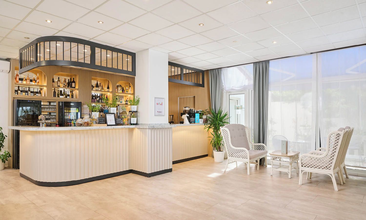 Een hotellobby met een gebogen receptiebalie, een zithoek met rieten stoelen en grote ramen.