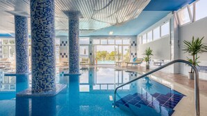 Une piscine intérieure agrémentée de colonnes carrelées, de rampes en verre transparent et de plantes en pot.