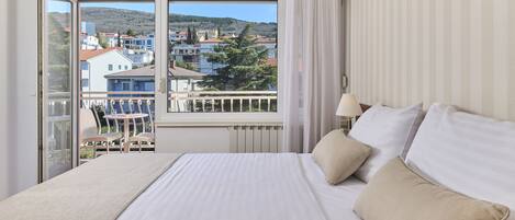 A hotel room with a large bed, a view of the city through a balcony, and a window with curtains.