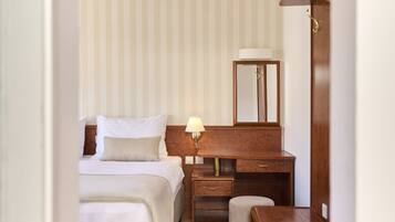 Una camera d'albergo con un letto, un comodino con una lampada, uno specchio e una scrivania in legno.