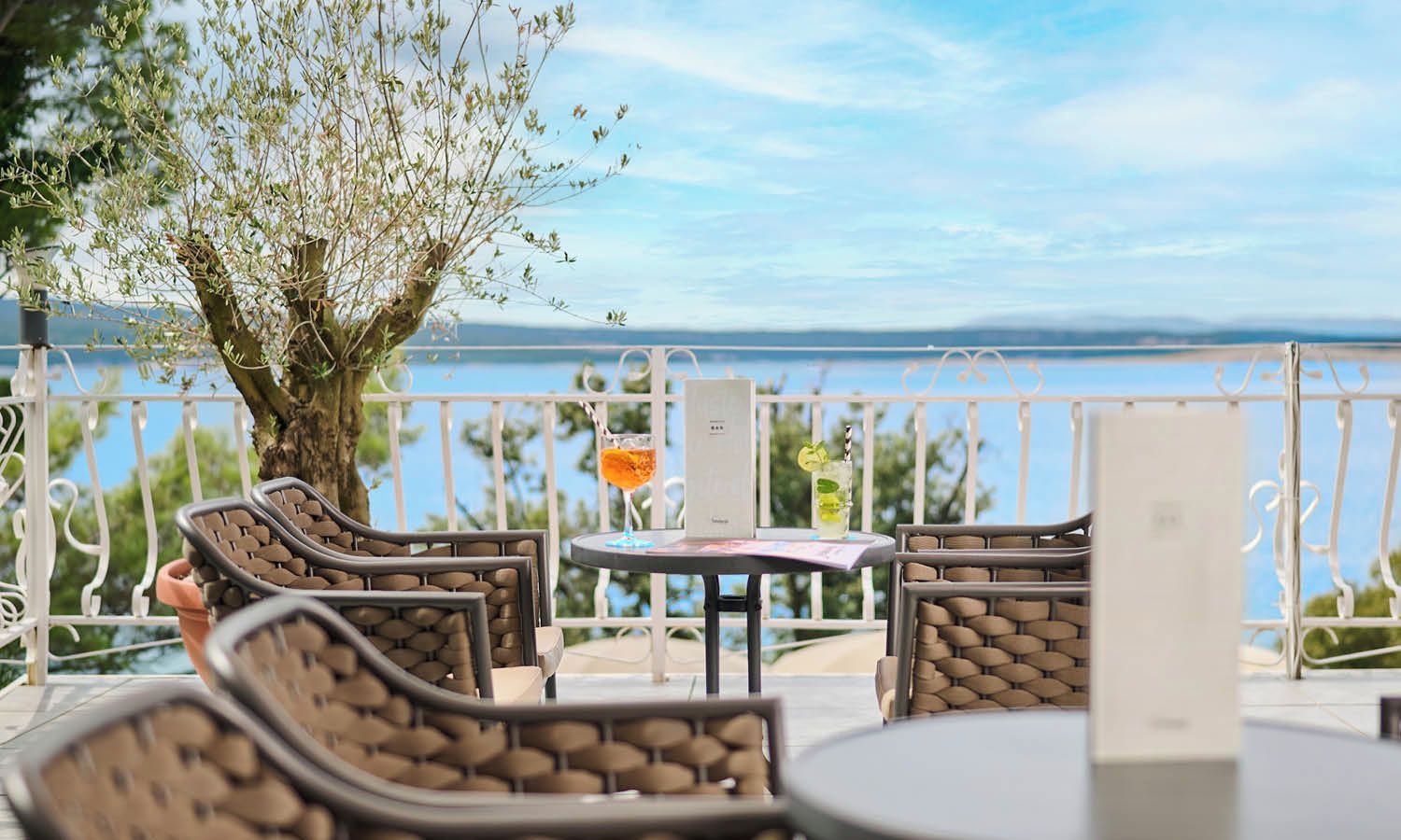 An outdoor seating area with wicker furniture, a table with a menu, and a view of the sea.