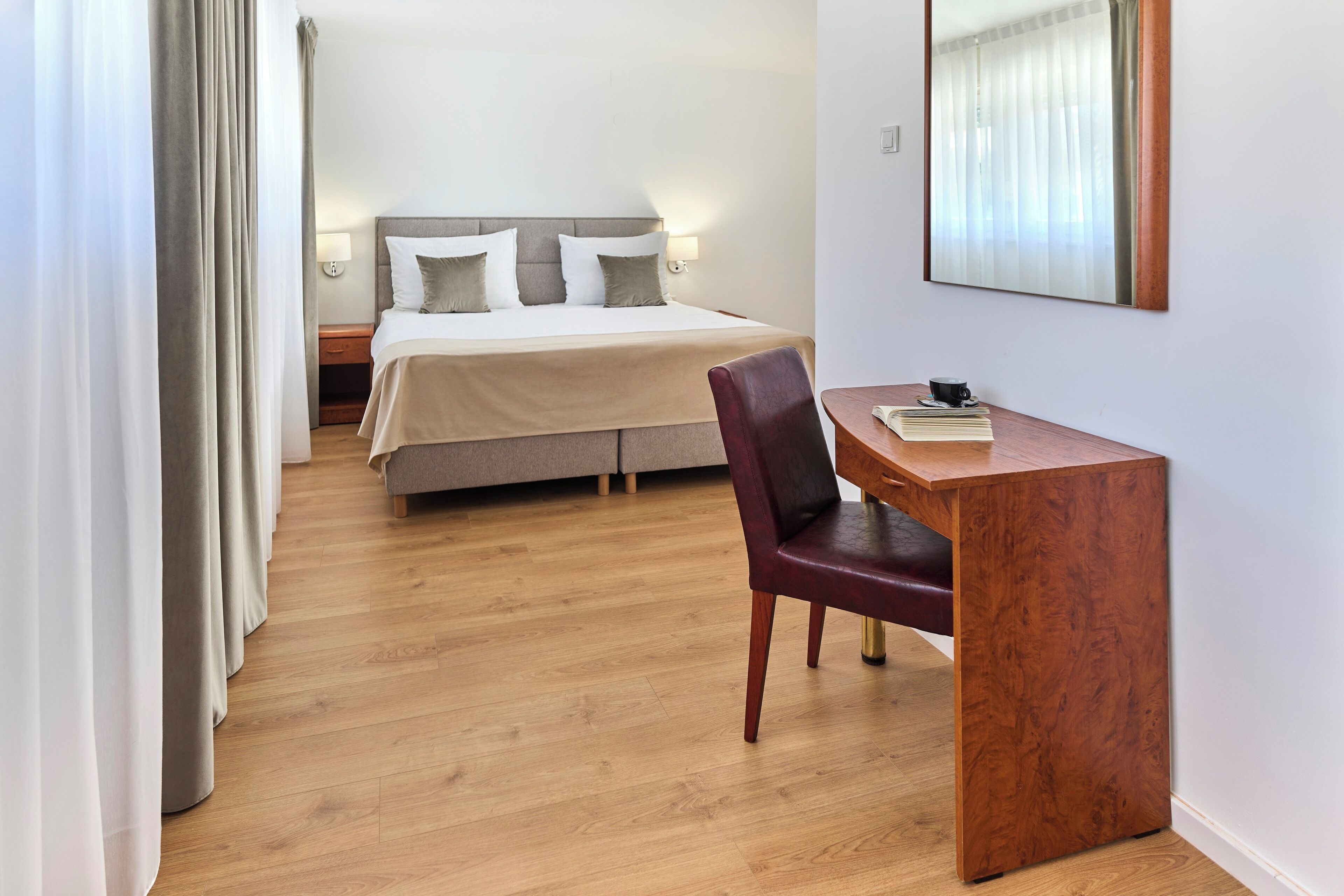 A hotel room with a bed, a desk, a chair, and a mirror.