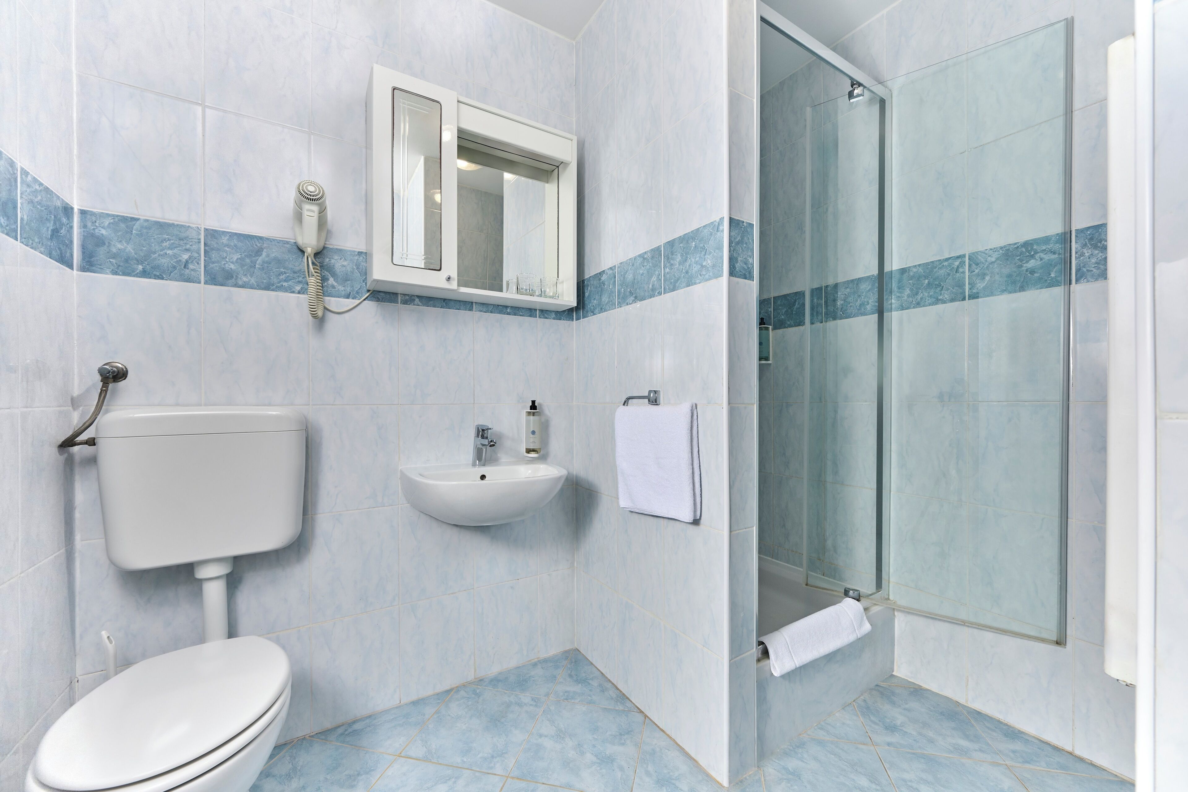 A bathroom with a toilet, sink, and glass shower enclosure.