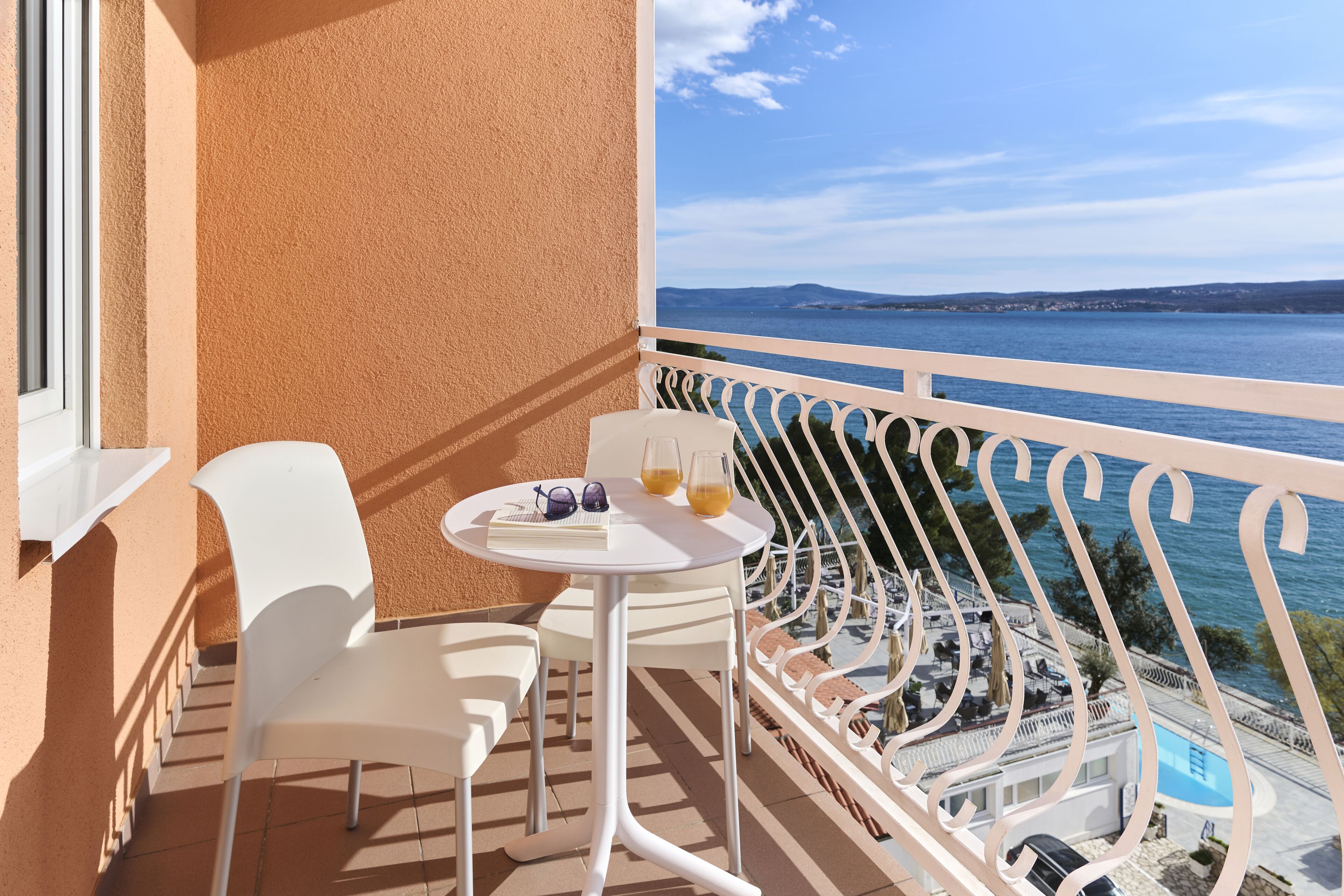 A balcony with white chairs and a table, overlooking a body of water and a distant landscape.