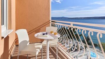 A balcony with white chairs and a table, overlooking a body of water and a distant landscape.