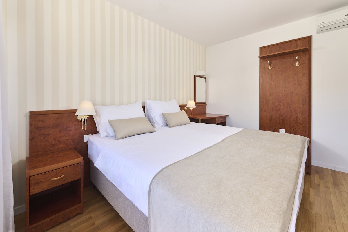 Une chambre à coucher bien rangée, avec un grand lit, des tables de chevet en bois, une table de chevet, une armoire et un miroir au mur.