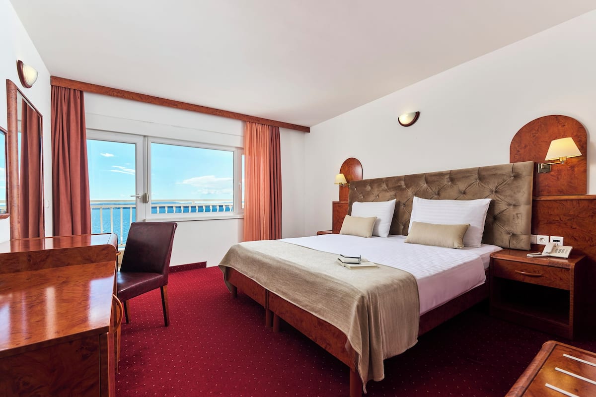 Une chambre d’hôtel avec un grand lit, un bureau, une chaise et une vue sur la mer.