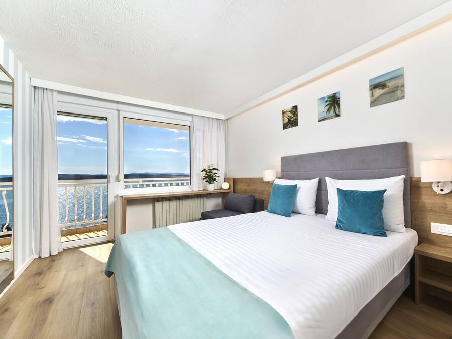 Une chambre d’hôtel avec un grand lit, une vue sur la mer depuis un balcon et une tête de lit en bois.