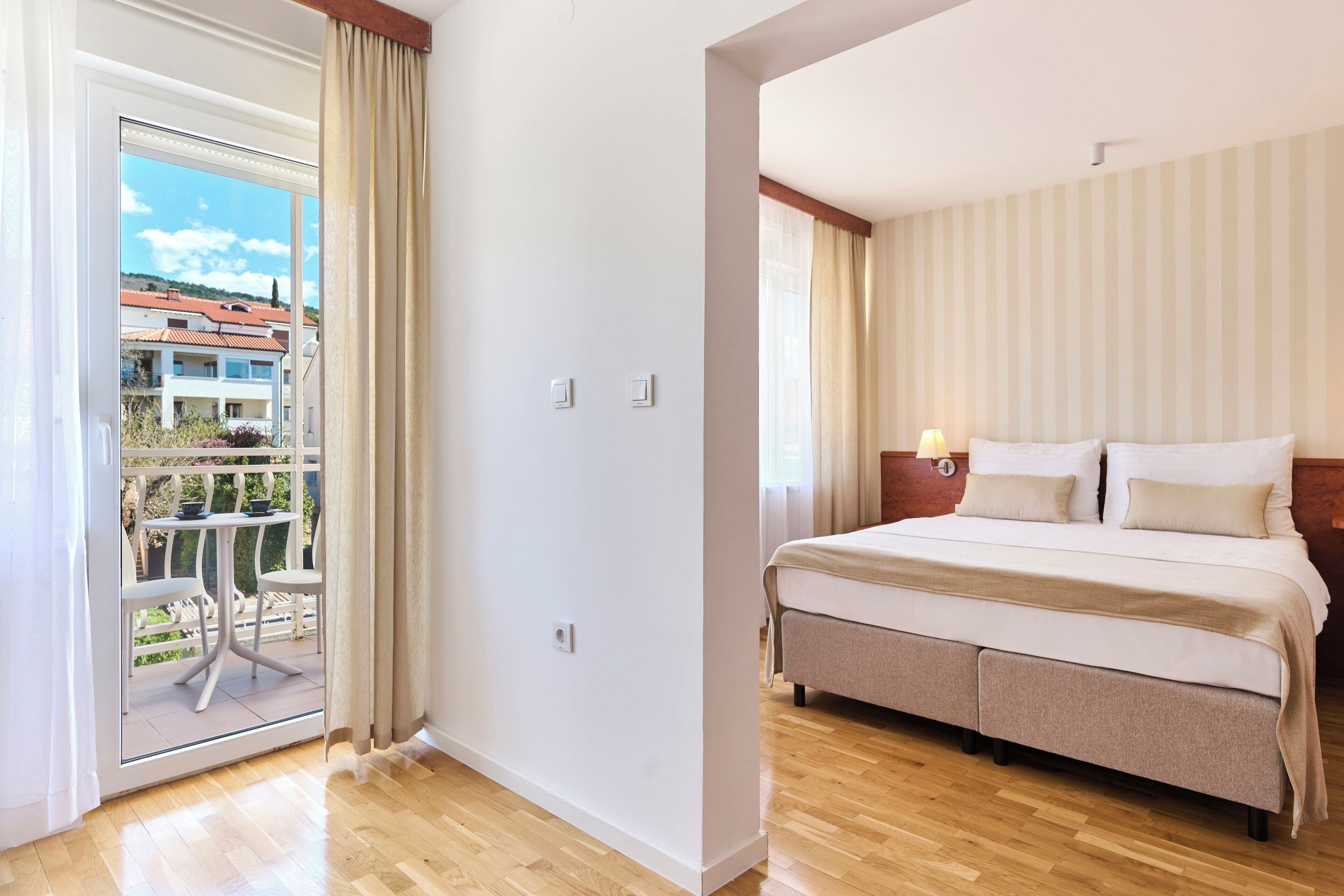 Habitación de hotel con cama, mesita de noche, una mesa con sillas y vistas al exterior.