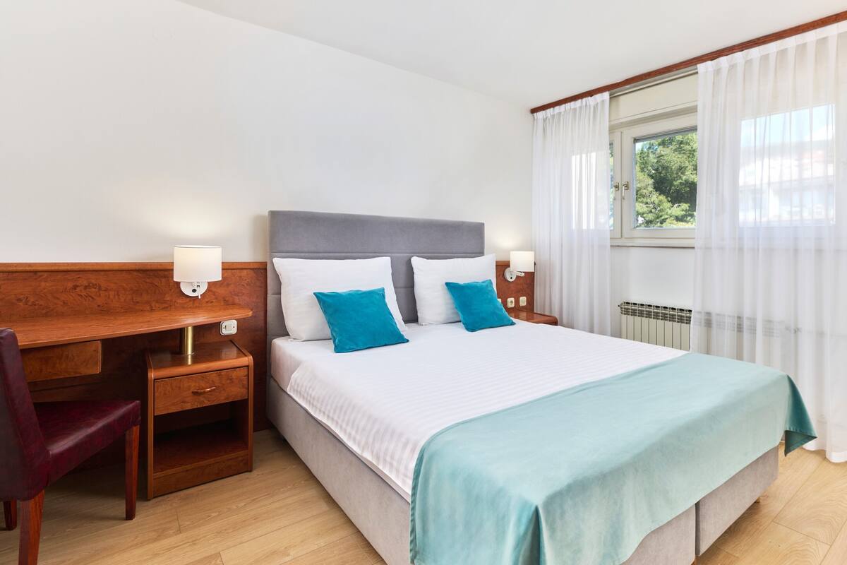 Une chambre d’hôtel avec un lit, un bureau, une chaise et une fenêtre avec des rideaux.
