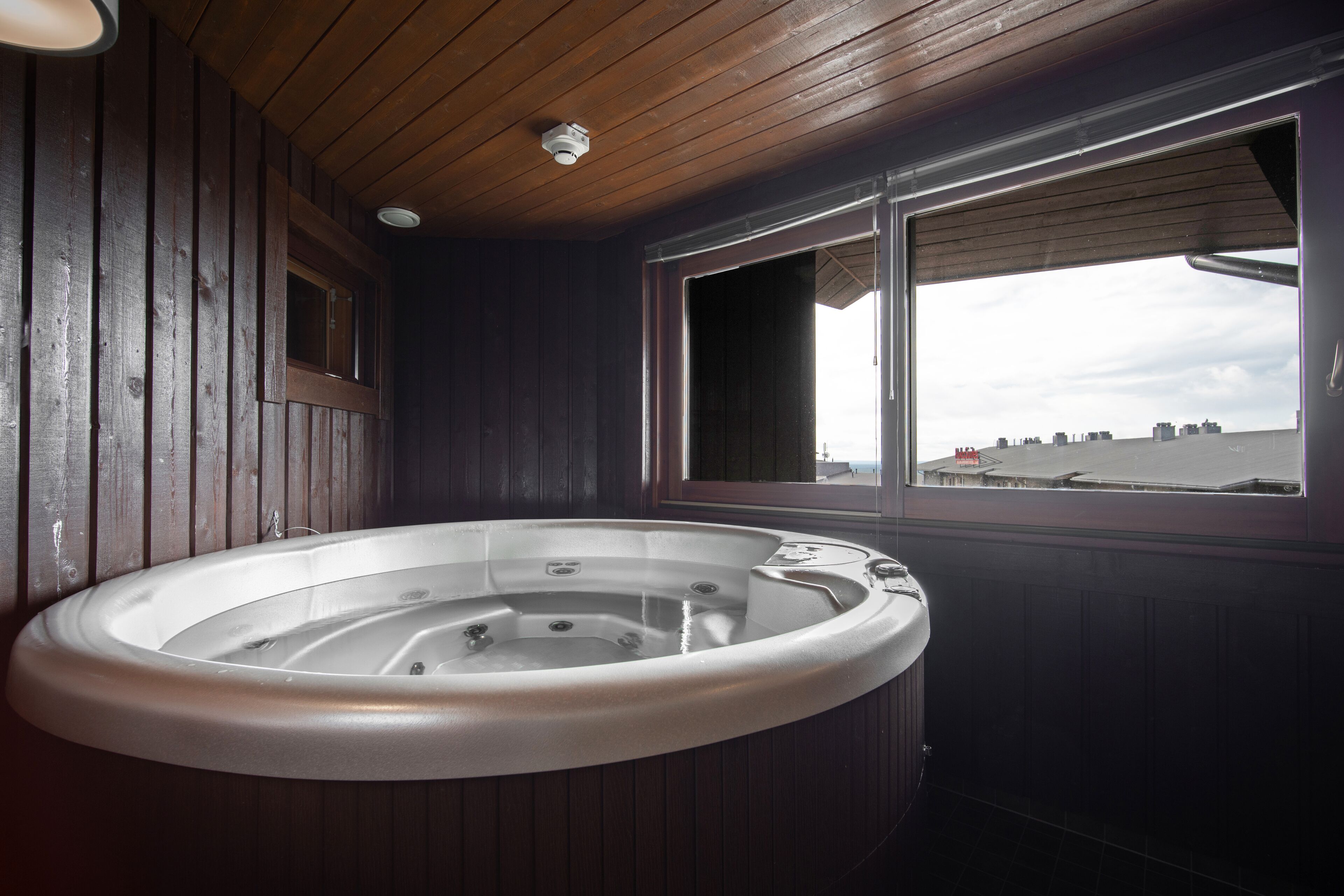 Un jacuzzi en una habitación con paredes de madera y ventana con vistas a un paisaje urbano.