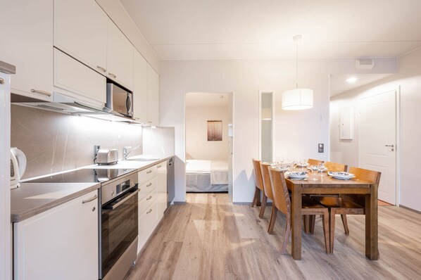 A modern kitchen with white cabinets, a microwave, and a dining area with a wooden table and chairs. - Ski-Inn RukaVillage (Kuusamo)