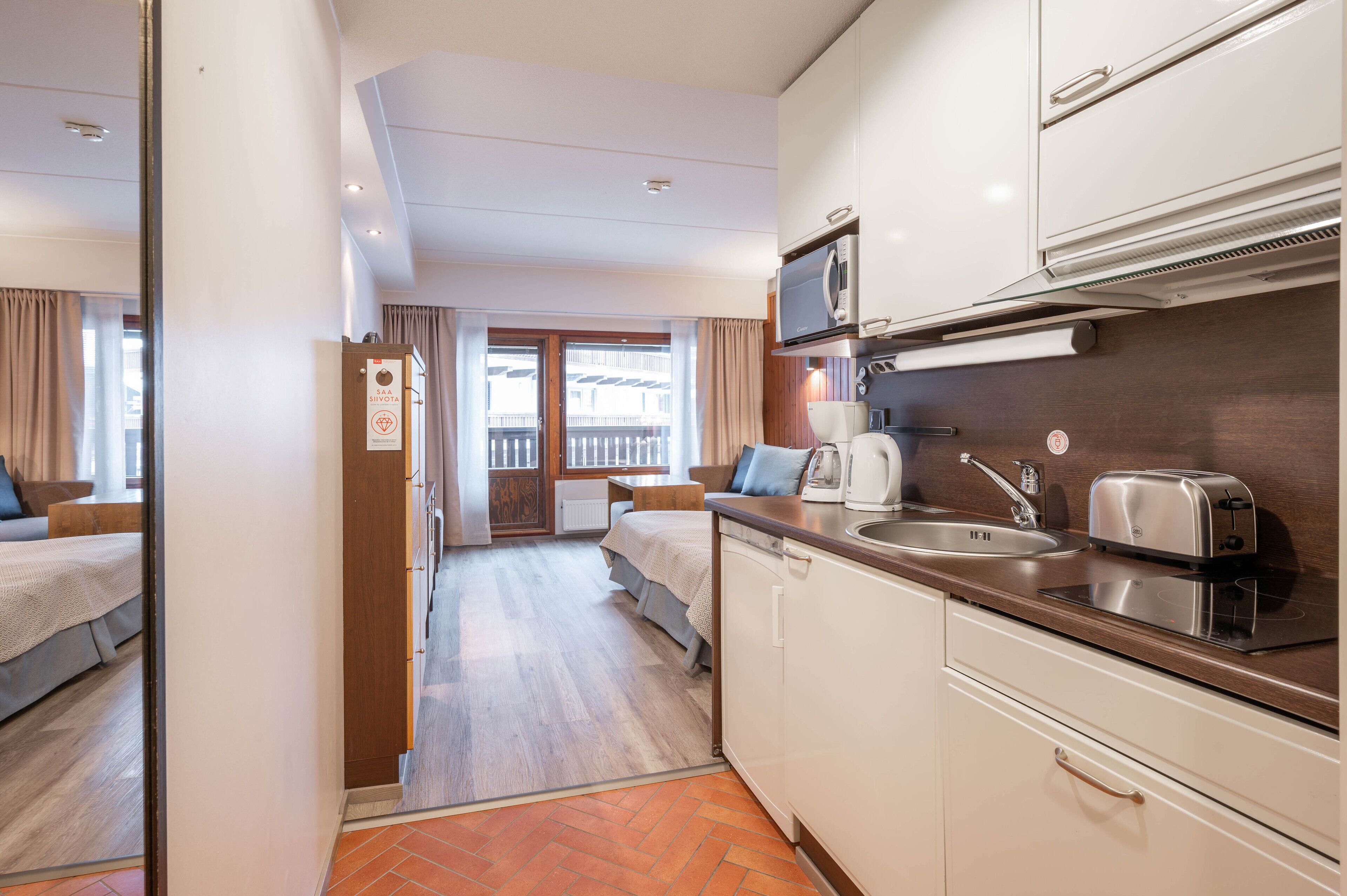 A compact hotel room with a kitchenette, a bed, a small sitting area, and a balcony with a view.