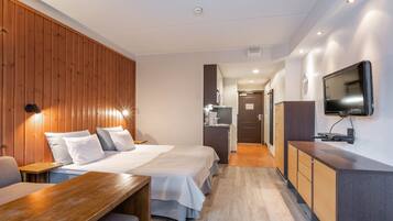 Ein Hotelzimmer mit zwei Betten, einer Holzwand, einem Schreibtisch, einem Fernseher und einer Küchenzeile.
