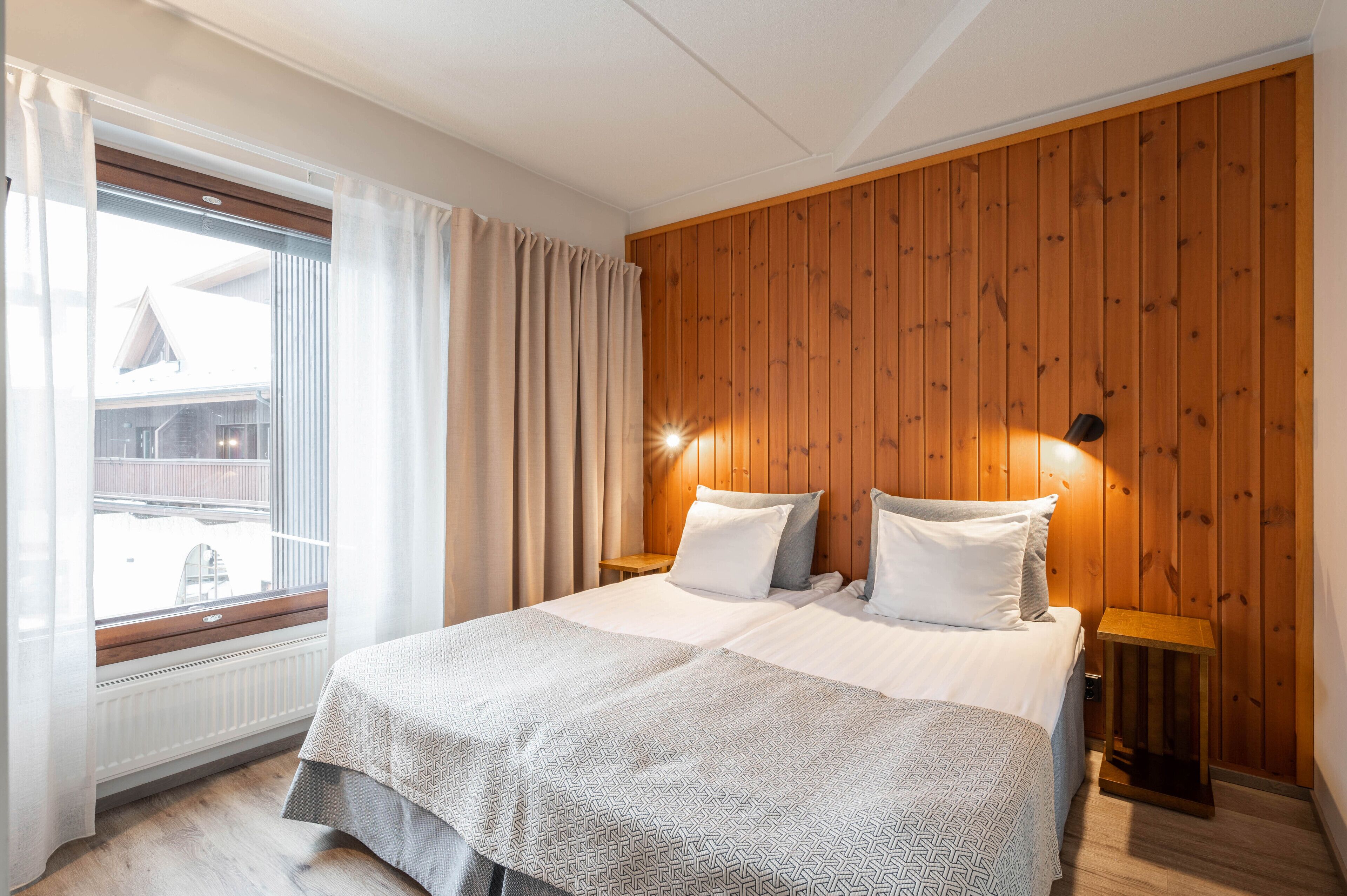 Un dormitorio con una cama grande, paredes de paneles de madera, una ventana con cortinas y una mesita de noche con una lámpara.
