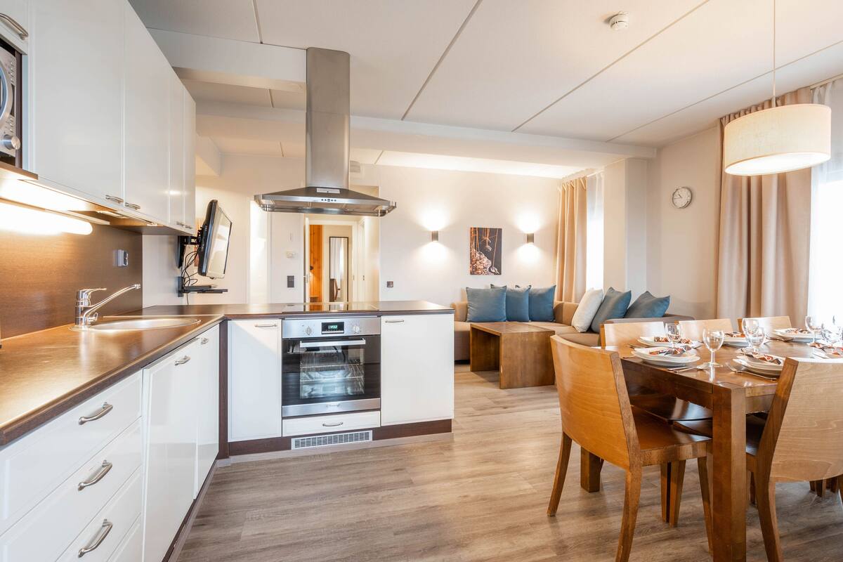 A modern kitchen with built-in appliances, a dining area with wooden furniture, and a cozy living space with a sofa and cushions.
