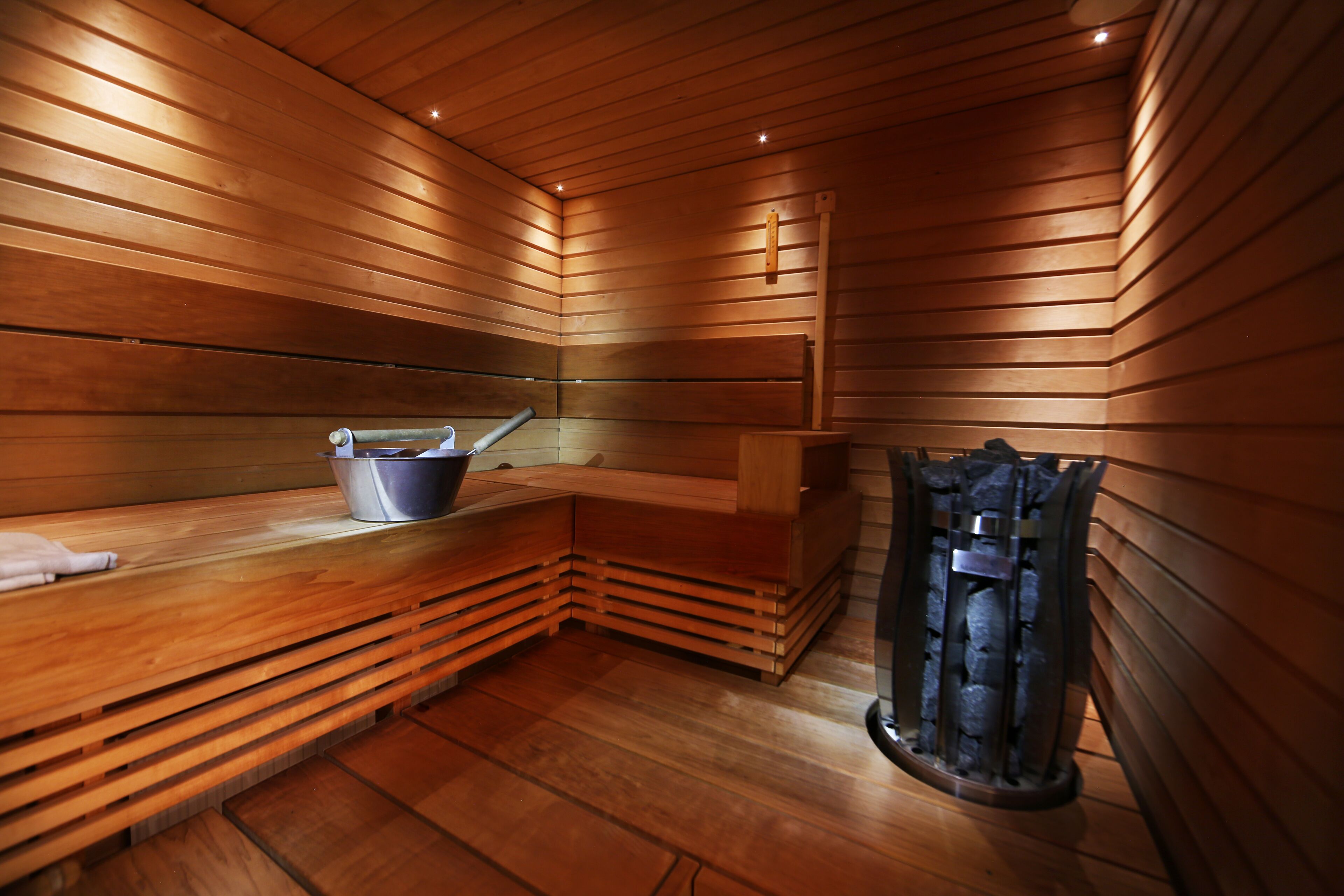 A sauna with wooden walls and benches, a bucket, and a stone heater.