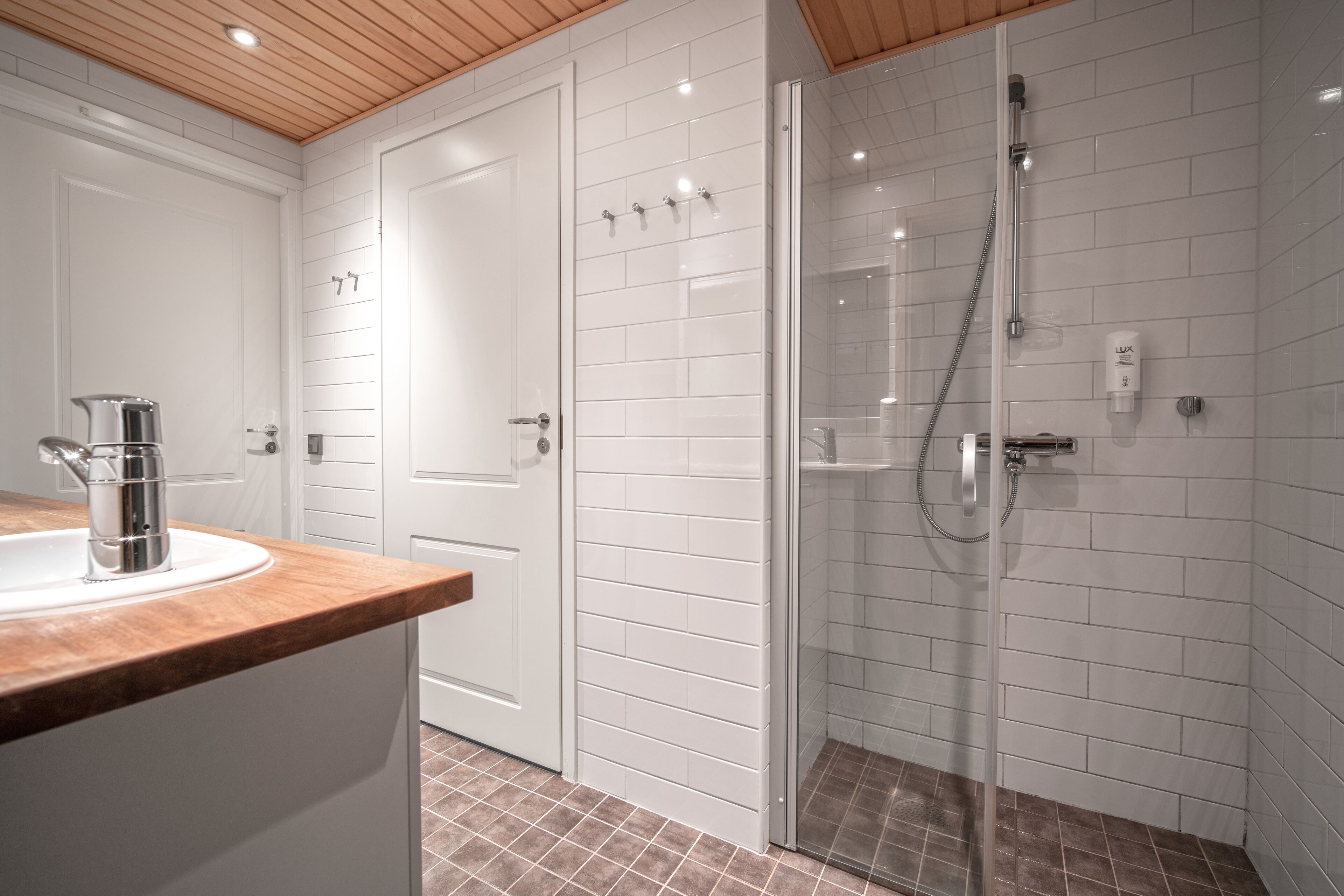 Un baño moderno con ducha de vidrio, paredes de azulejos blancos y encimera de madera con lavamanos.