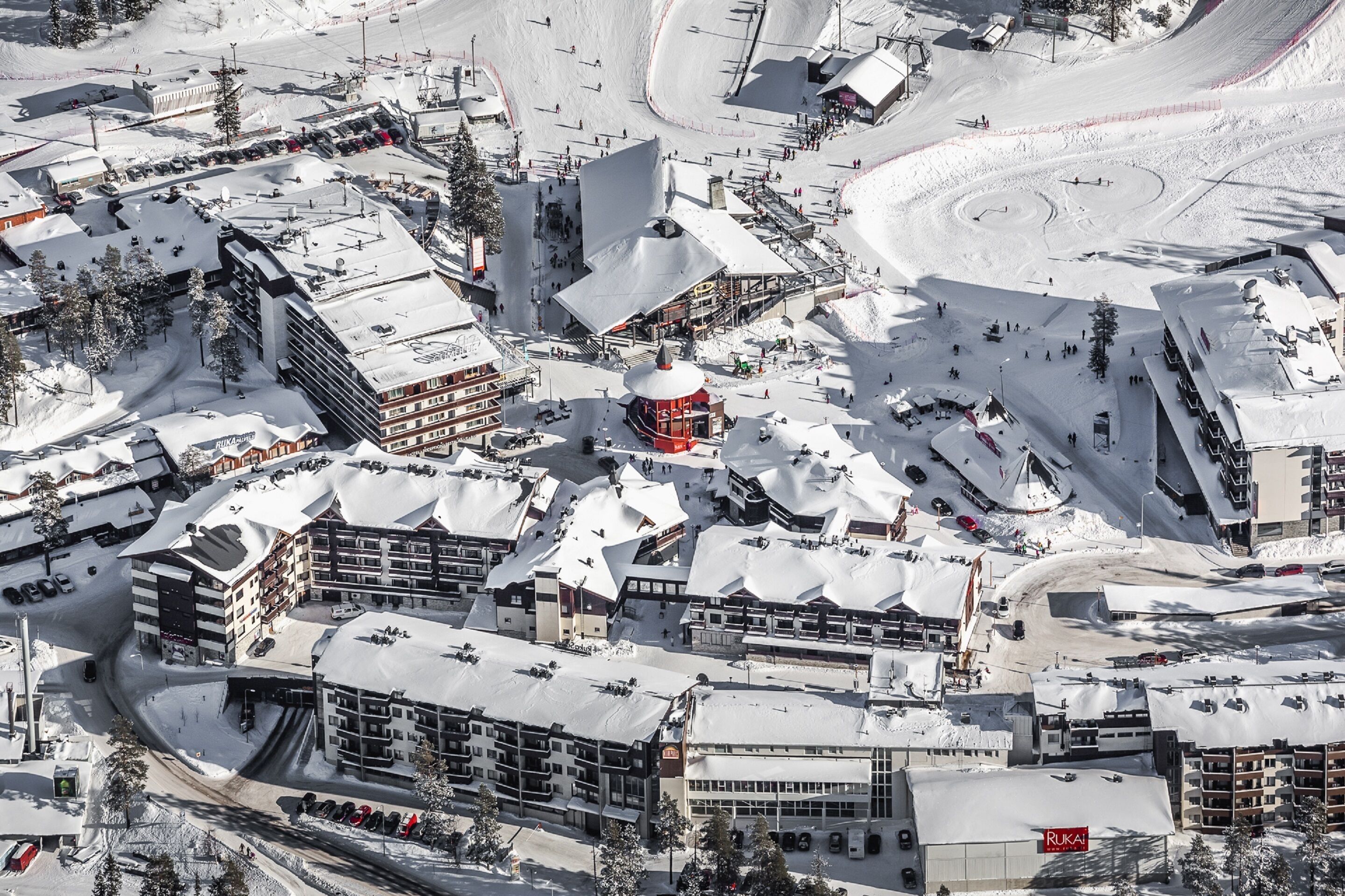 A snow-covered ski resort with multiple buildings, including a prominent red structure, and a winding ski slope.